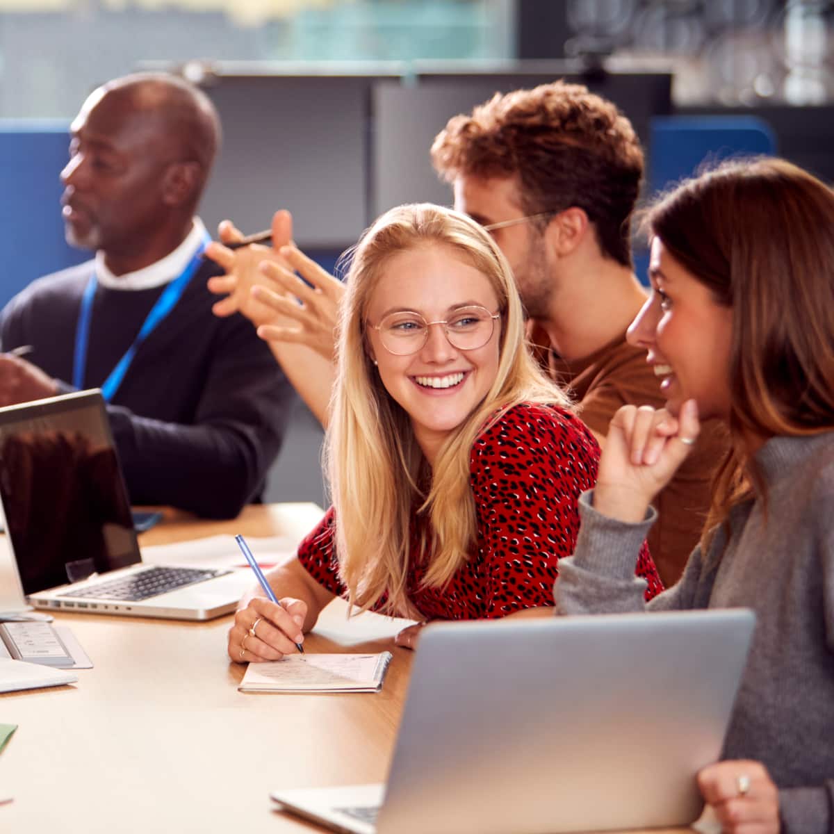 Eight people sitting around desk smiling working together laptop paper pen. 