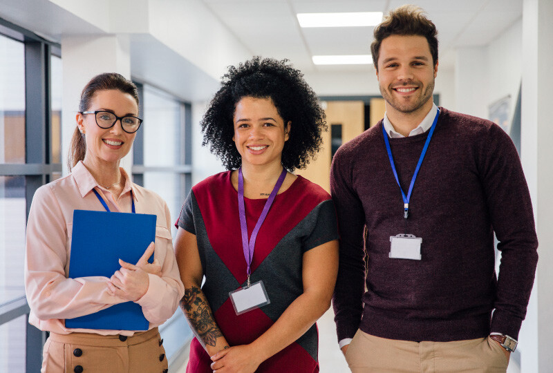 Three coworkers standing side by side in school hallway smiling and facing forward.