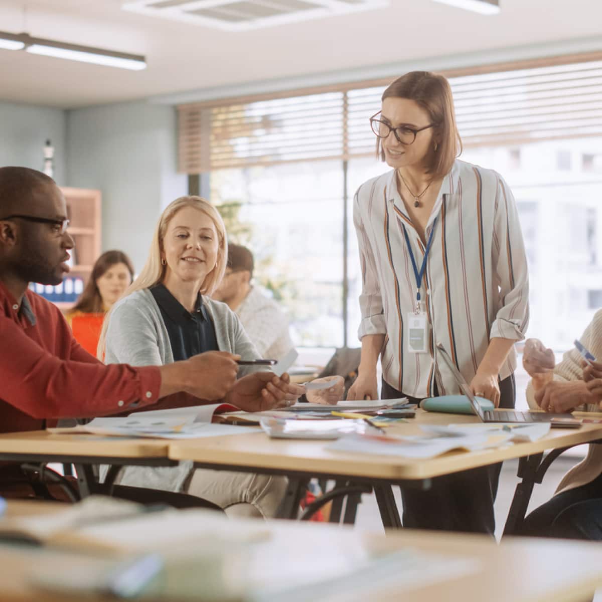 Five teachers sitting in classroom around desks working together. 