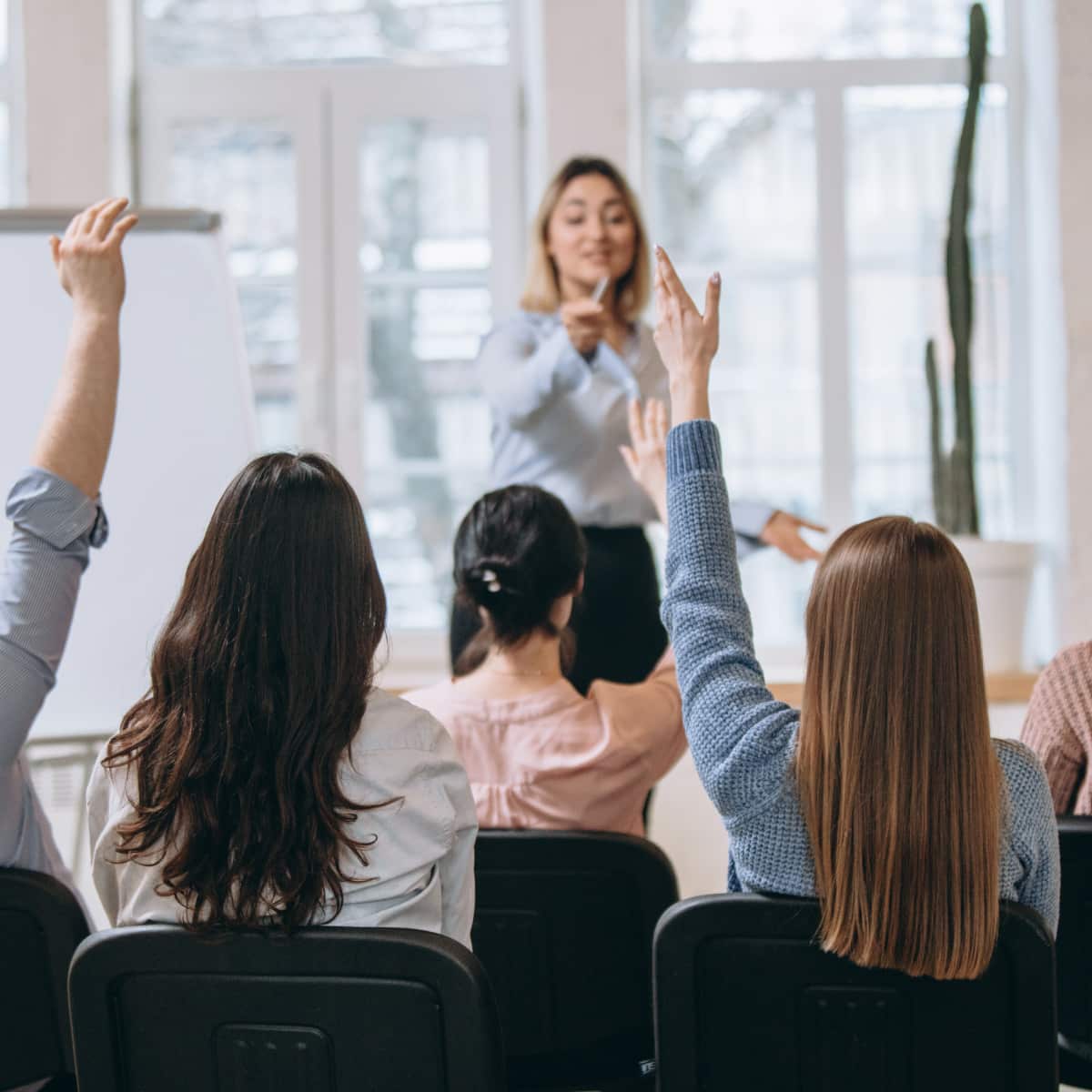 Six people sitting in chairs listening to presenter four people raising hands asking questions. 