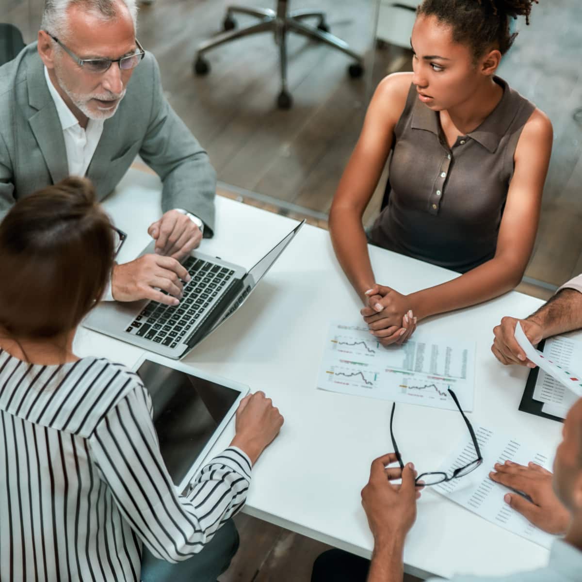 Top view of five colleagues around desk in conference room working together. 