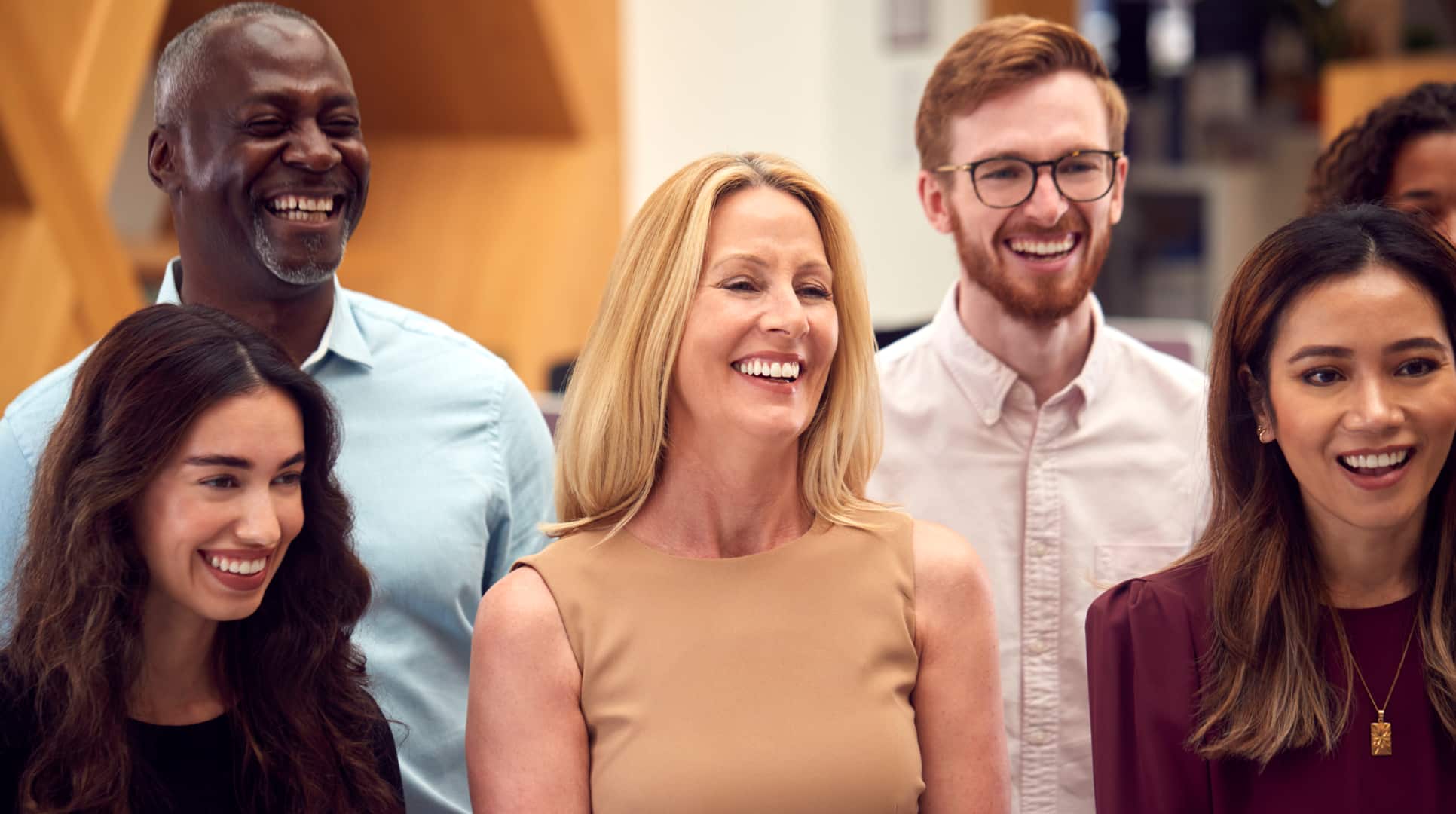 Six people standing next to each other smiling laughing looking forward. 