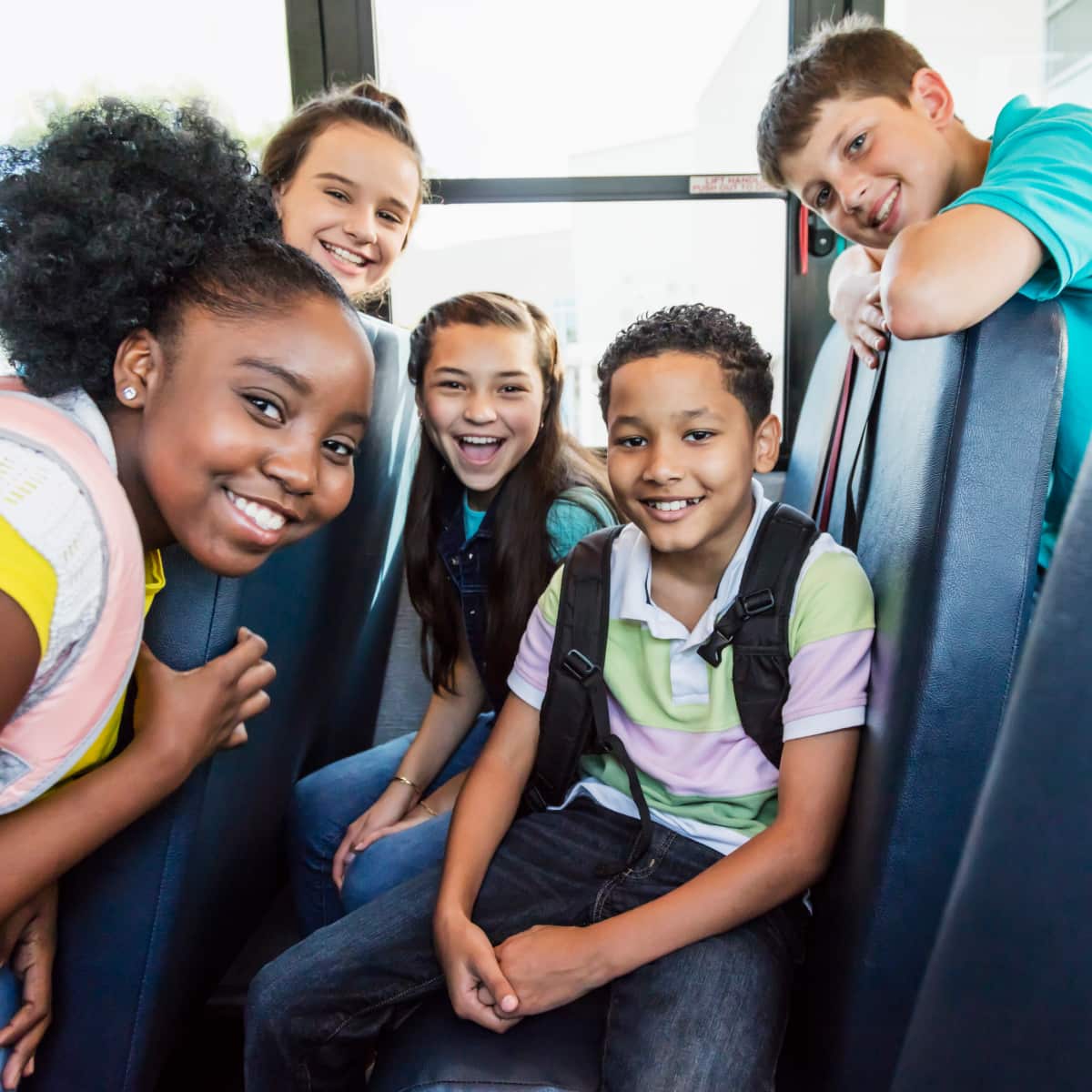 Five students smiling on school bus. 