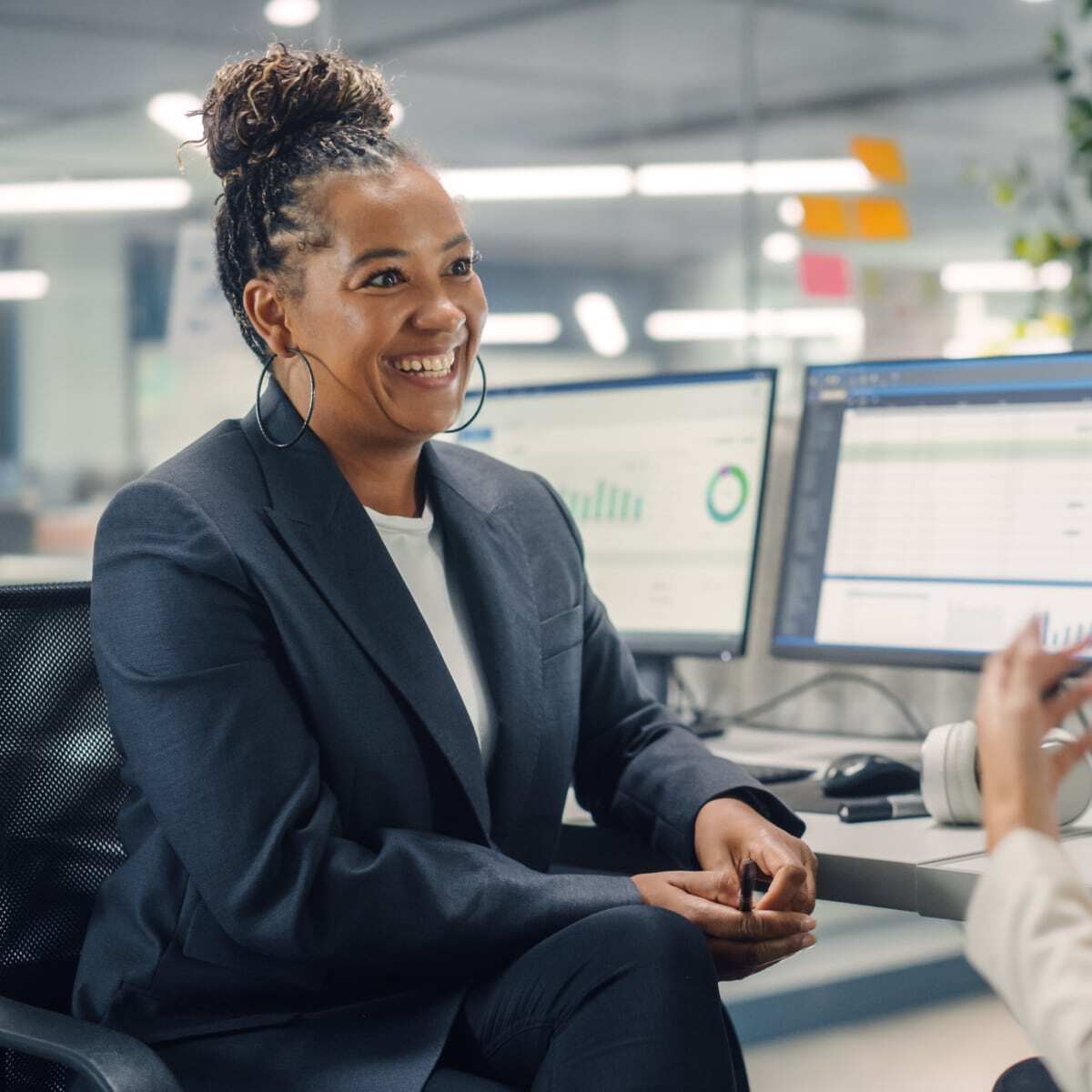 Two co workers sitting at desk facing each other smiling communicating.