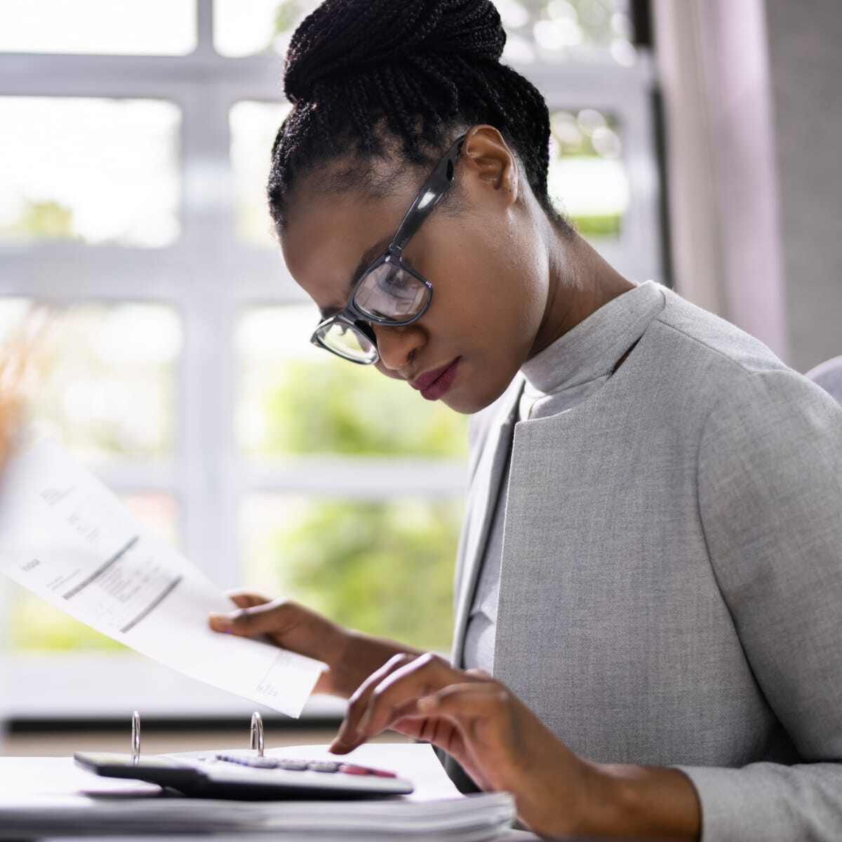 Business woman working at desk in office using calculator computer paper and pen. 