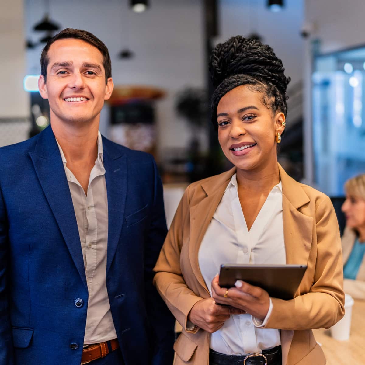 Two co workers standing side by side in conference room facing forward and smiling. 