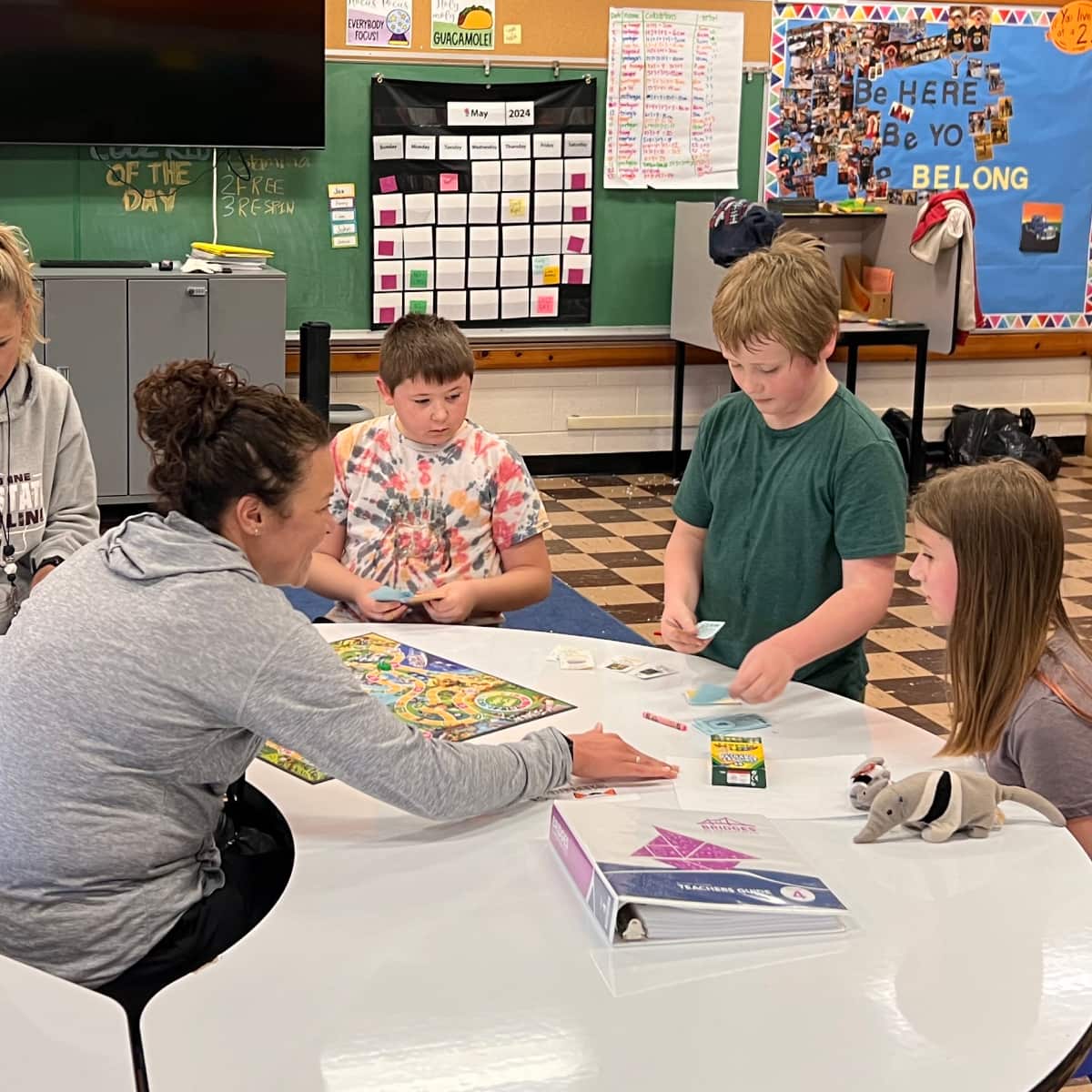 Three students sit at desk in classroom learning from two teachers. 