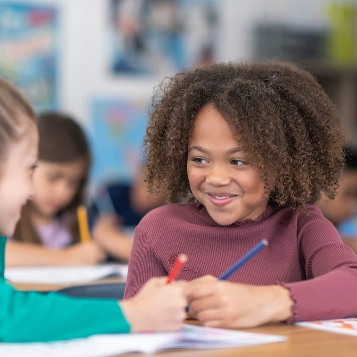 Two students sitting as desk in school classroom holding pencil working together. 