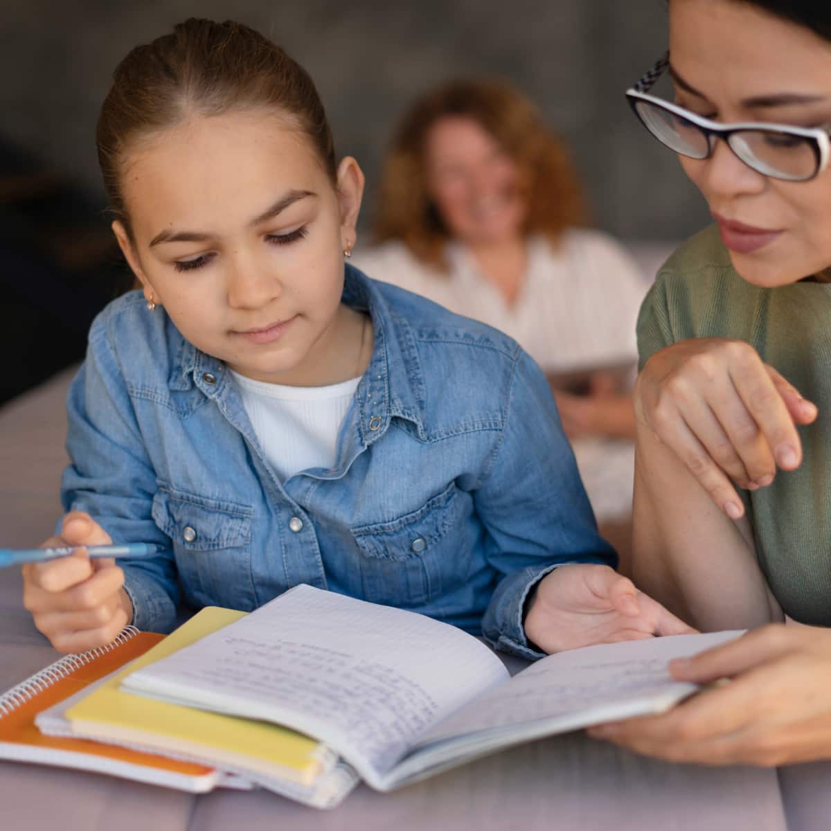 Student and teacher sitting at desk reading book together. 