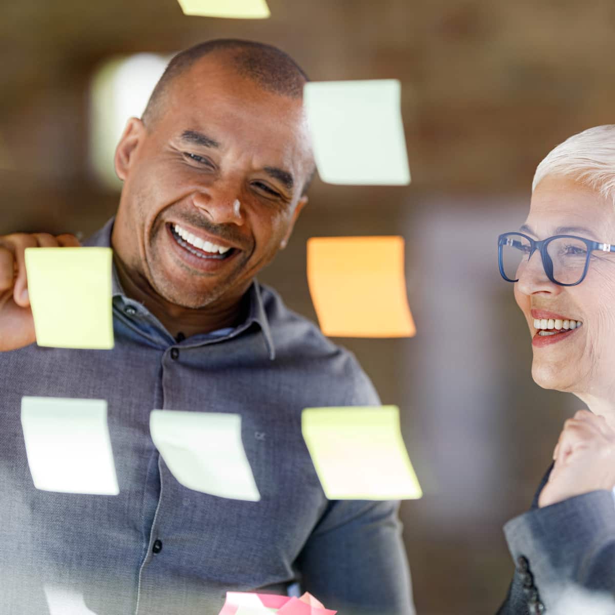 Two co workers smiling working together looking at sticky notes on board. 