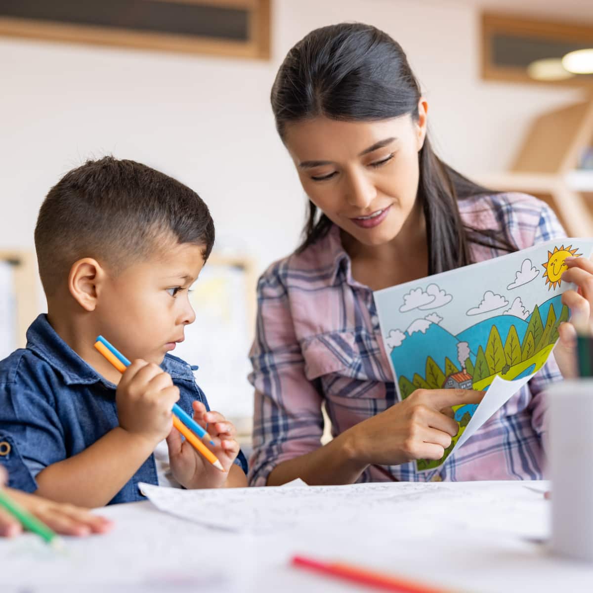 Teacher and student sitting around table in classroom looking at a painting. 