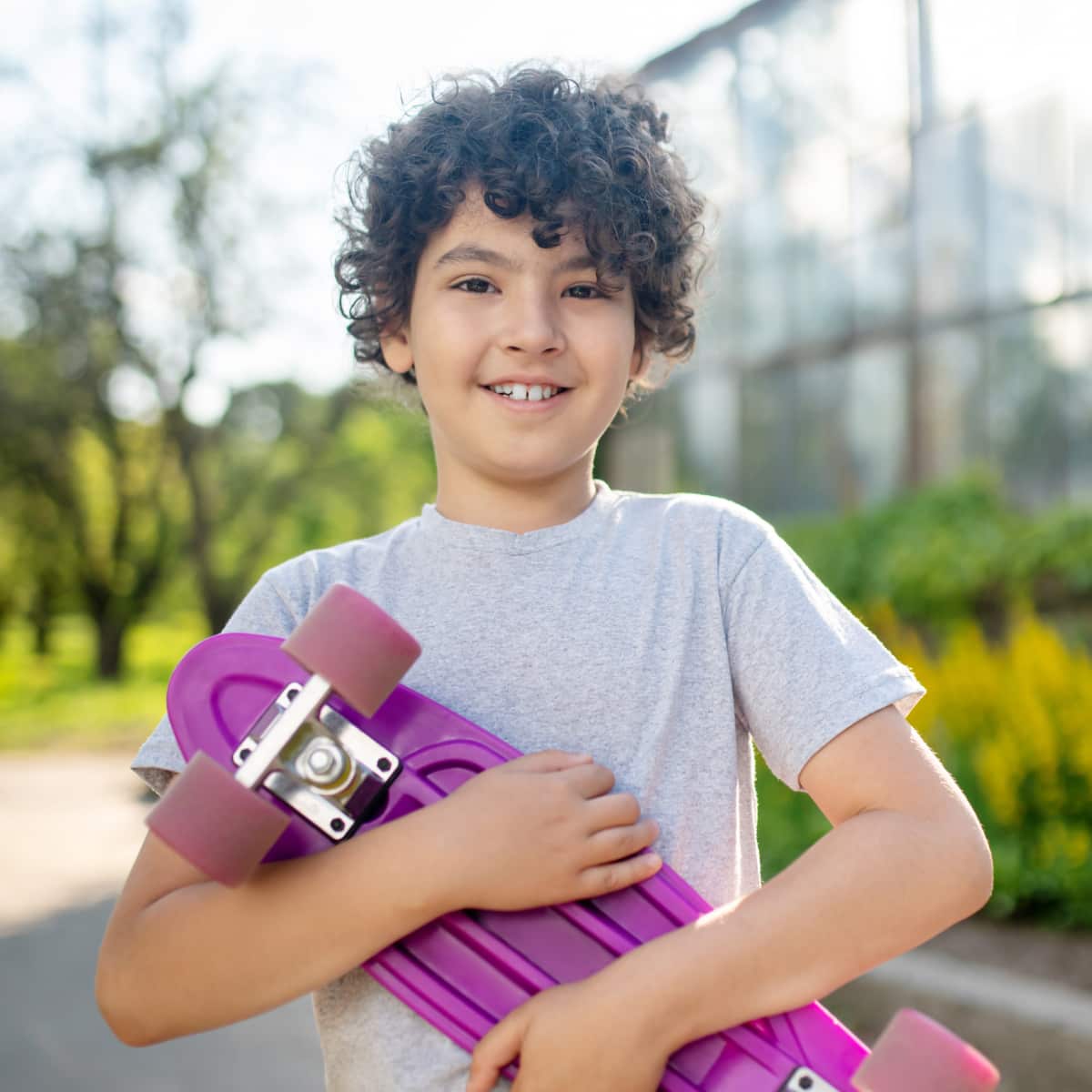 Boy smiling standing outside holding skateboard. 