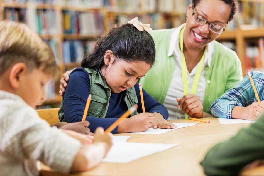 Teacher smiling with students writing.