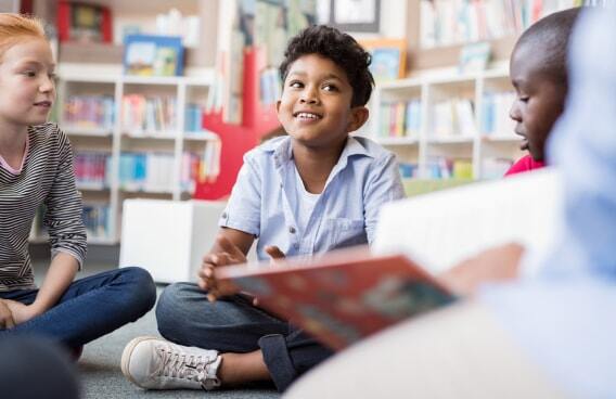 Kids congregated on the floor reading books and conversing with one another. 