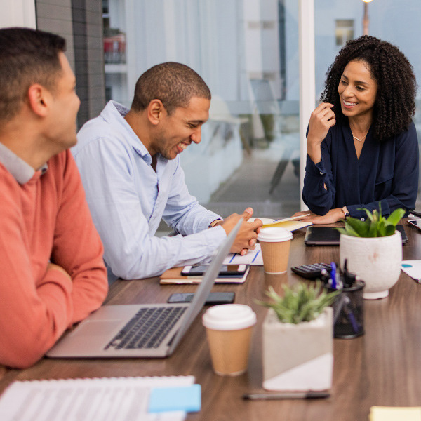 coworkers sitting around desk in conference room working together using laptops