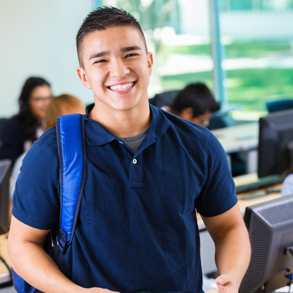 student standing facing forward smiling holding backpack in computer lab