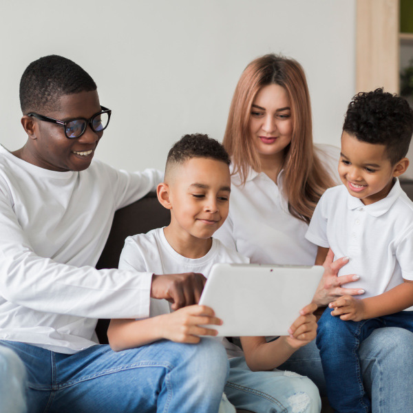 man woman two young boys sitting together on couch looking at tablet