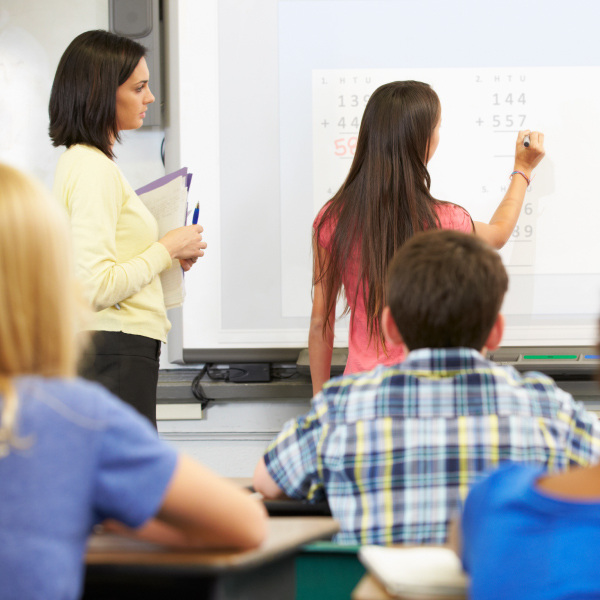 student standing front of class solving math problem on smartboard 