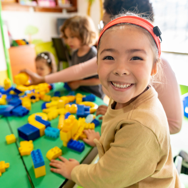 children sitting around table in classroom girl smiling playing with blocks