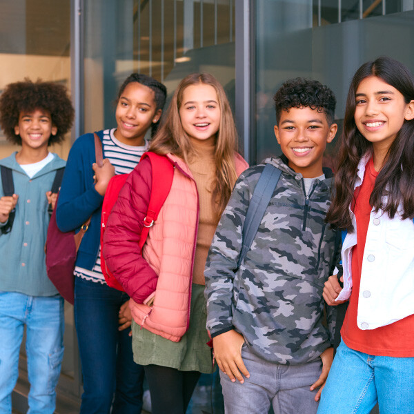 students standing in line next to each other facing forward smiling holding backpacks