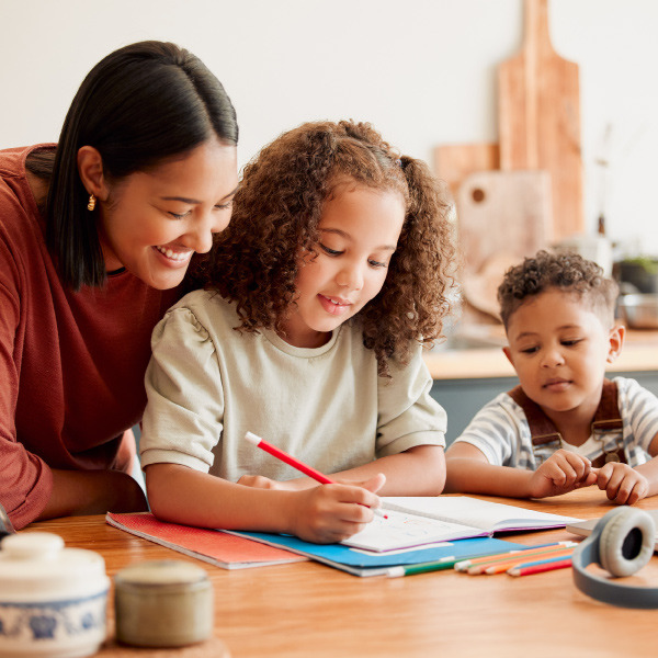 woman sitting with two children at table helping with homework