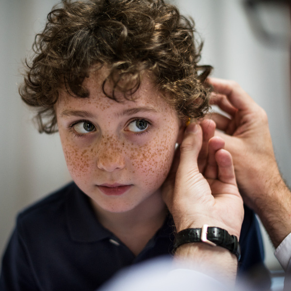 young boy sitting facing forward getting his ear checked out