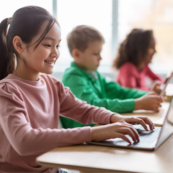 students sitting at desks in classroom typing on laptop