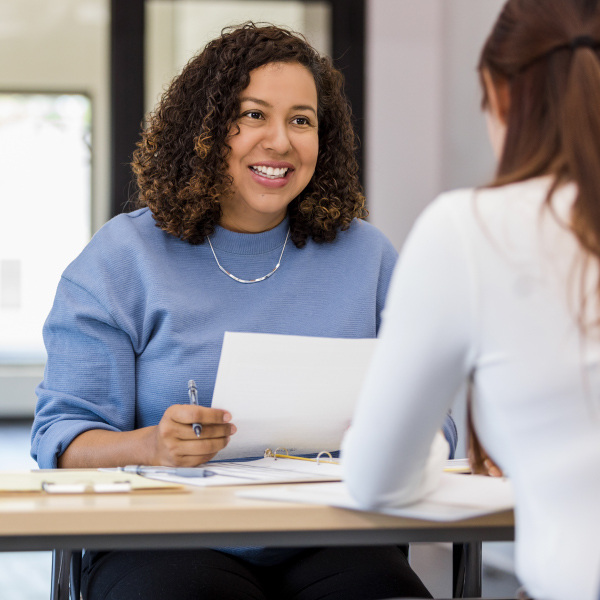 two co workers facing each other sitting at desk communicating looking over documents