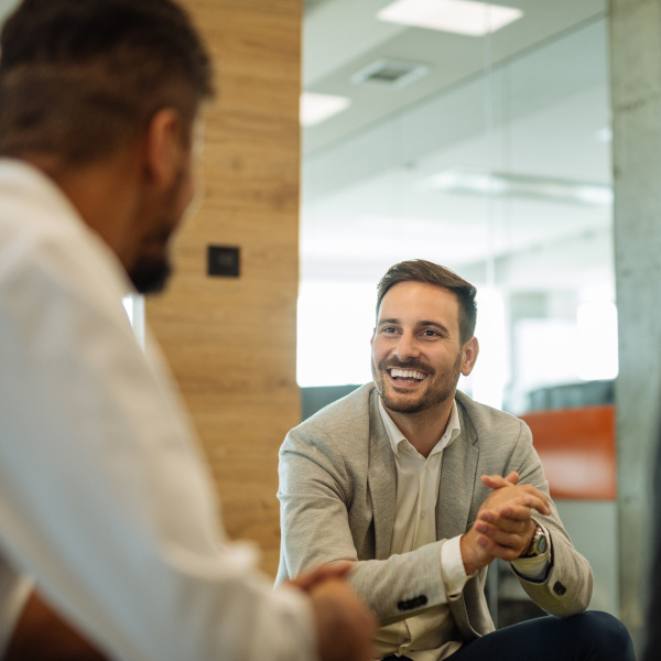 two coworkers sitting in office facing each other communicating smiling