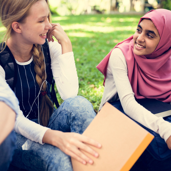 students sitting outside on grass holding backpacks smiling