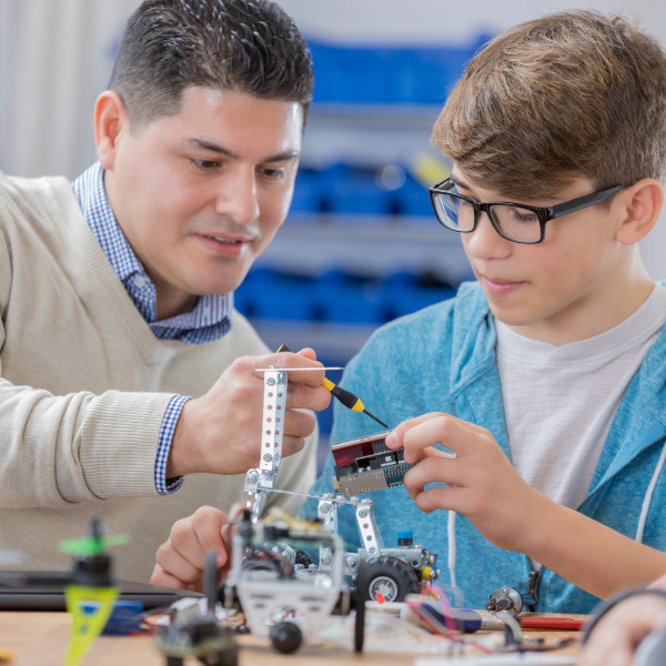 student and teacher sitting at desk in classroom working with robotics 