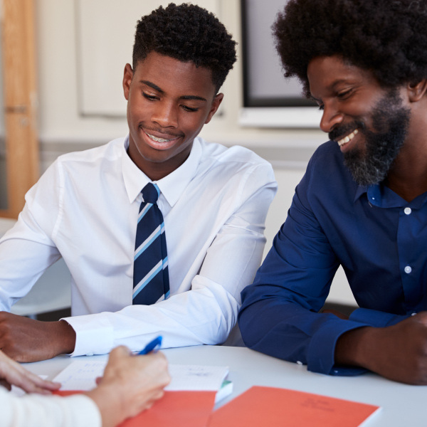 student and adults sitting at table facing each other smiling looking over documents