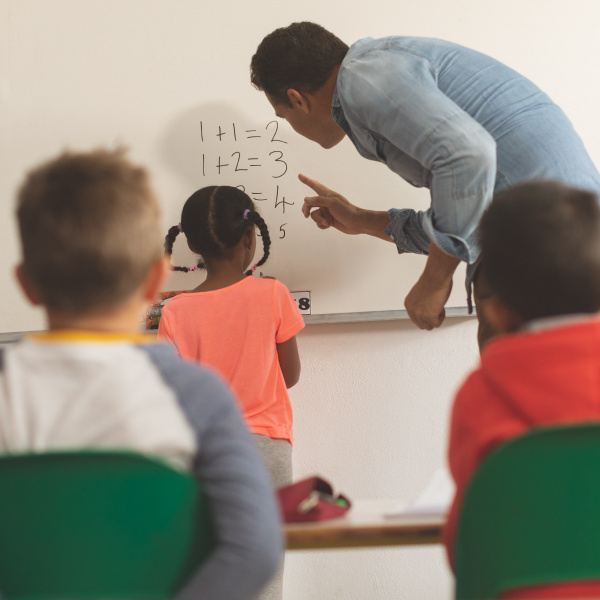 teacher and student standing working together front of class using whiteboard in classroom