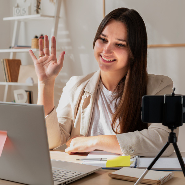 woman sitting at desk smiling looking at laptop waving for online meeting