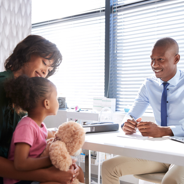 parent and child sitting across from teacher sitting at desk in office