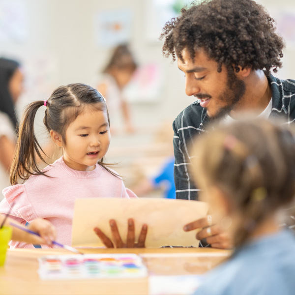 children and teacher sitting around table in classroom painting 