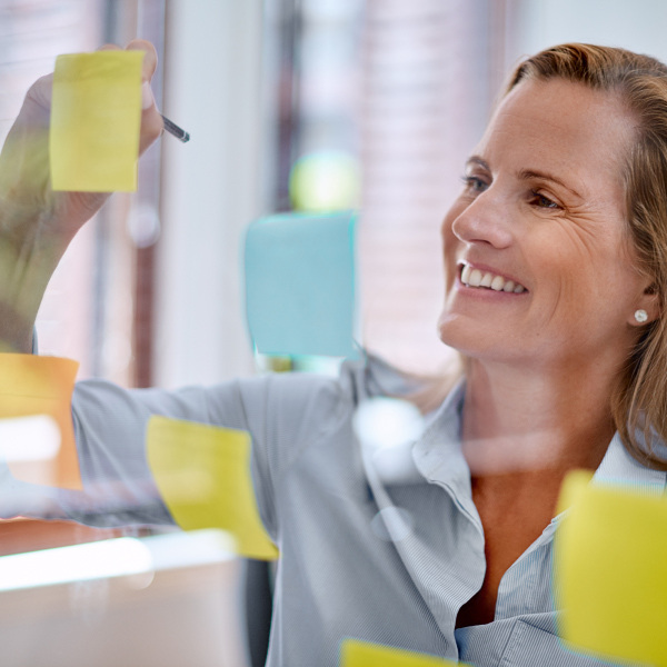 female standing smiling writing on sticky notes on board