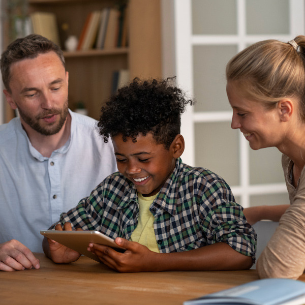 child and two adults sitting at table next to each other looking at tablet