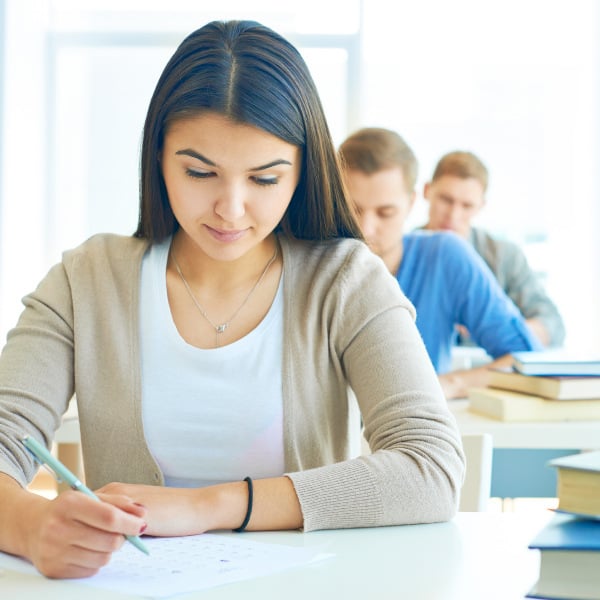 students sitting at desks in classroom holding pencils taking exam