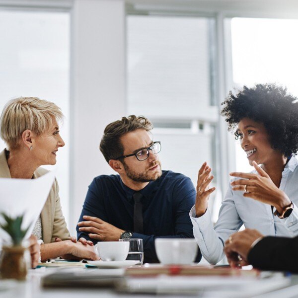 four coworkers sitting around table in conference room communicating working together