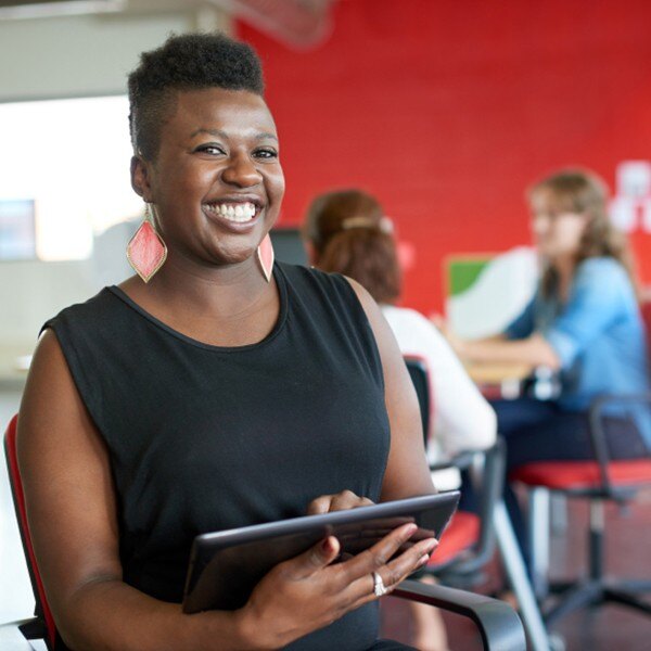 female worker sitting in office facing forward smiling holding tablet