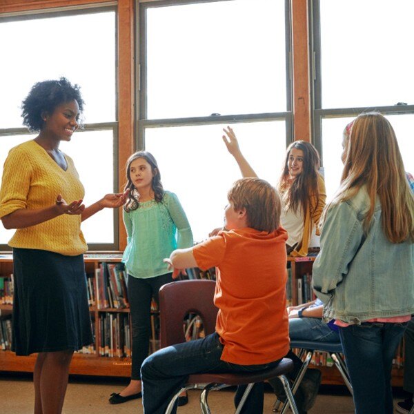 teacher talking to students in back of classroom one student raising their hand