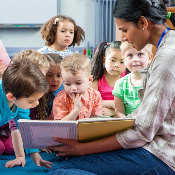 seven children sitting on classroom floor facing forward teacher reading book