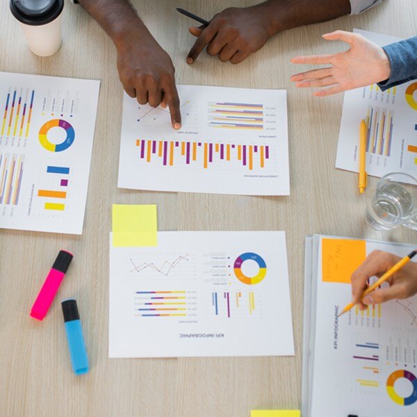 five documents with data charts on table four individuals working together