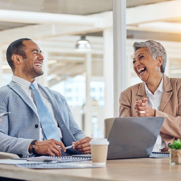 two co workers sitting at desk in conference room laughing working together