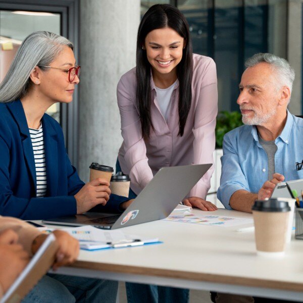 three coworkers sitting around table in office working together communicating laptop pens paper