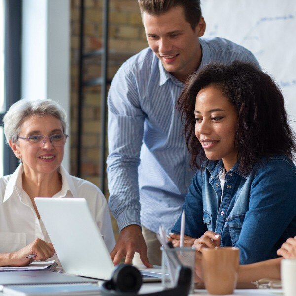 three coworkers in office around table working together communicating looking at laptop