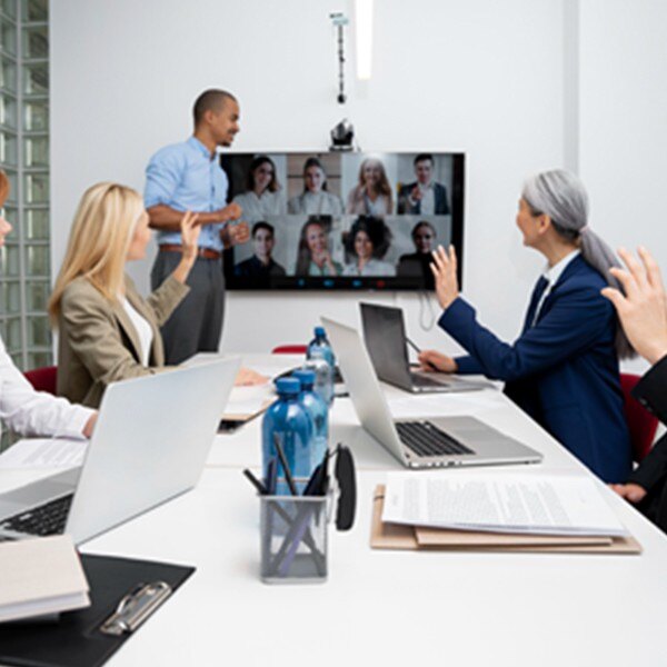 five coworkers in conference room in meeting with eight coworkers joining virtually