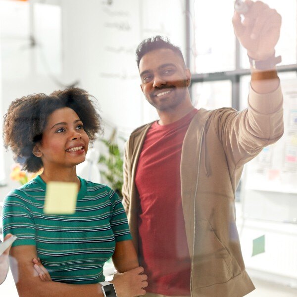 co workers standing side by side smiling working looking at dry erase board