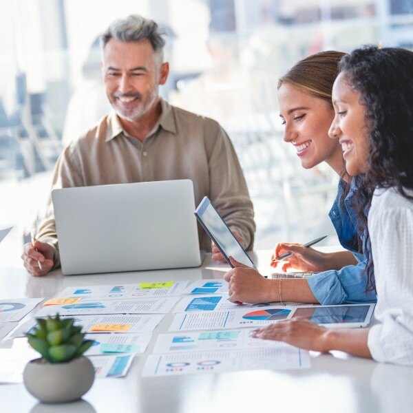 co workers sitting around table in conference room looking at documents with data smiling